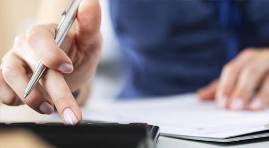 A woman's hand holding a pen and using a calculator