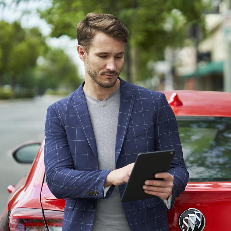 A man looking at his iPad behind a Buick red car.